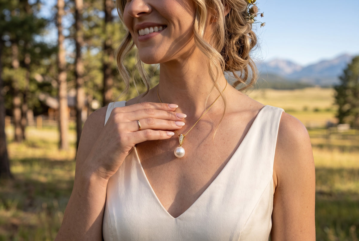 Trebor Style 18k gold Edison pearl pendant necklace with diamond accents worn by a woman in a white dress outdoors.