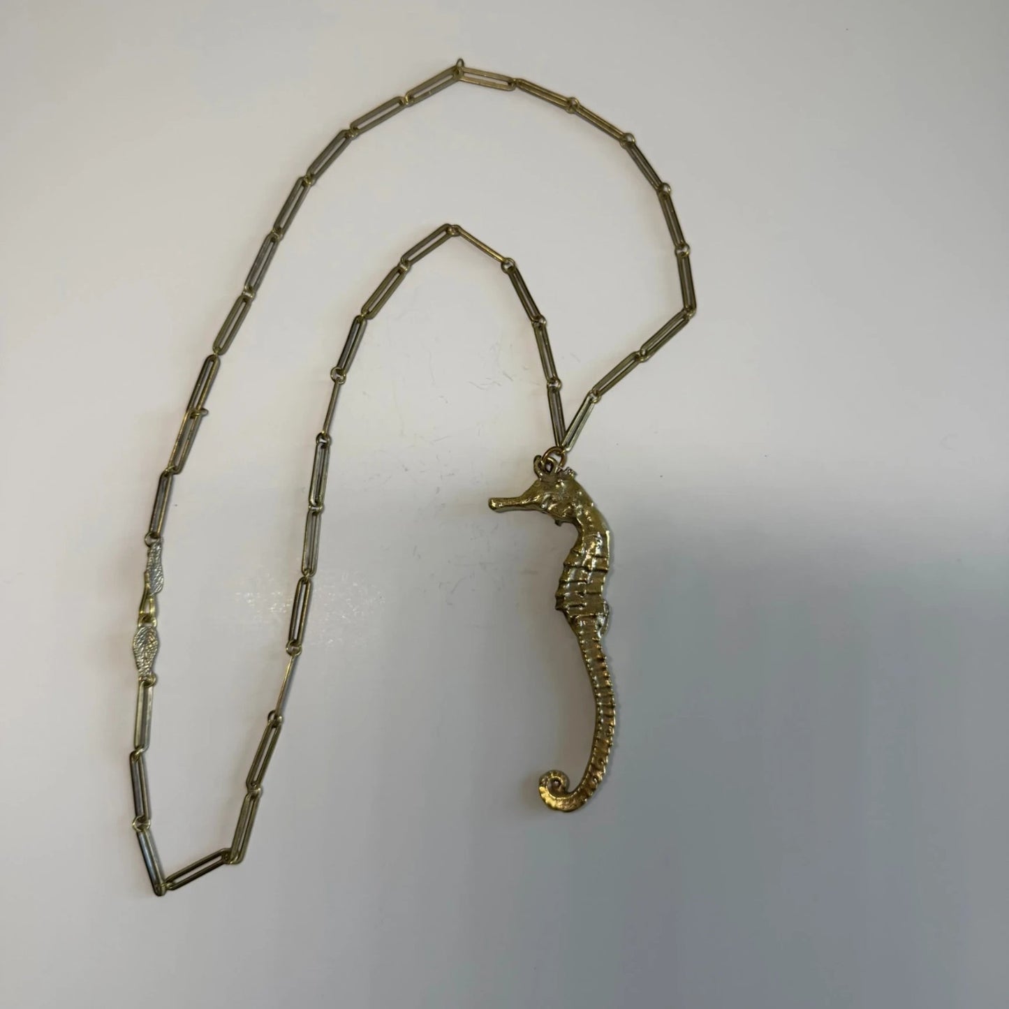 Trebor Style gold seahorse necklace with a unique leaf clasp detail on a delicate chain, symbolizing oceanic grace.