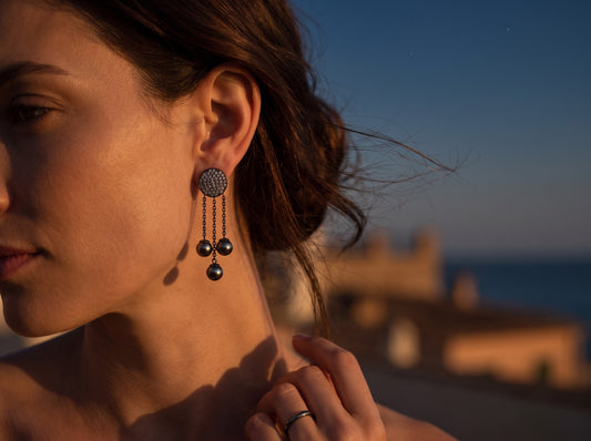Trebor Style Dyanne Belle pavé disc and triple chain drop earrings with black Tahitian pearls on a woman at sunset