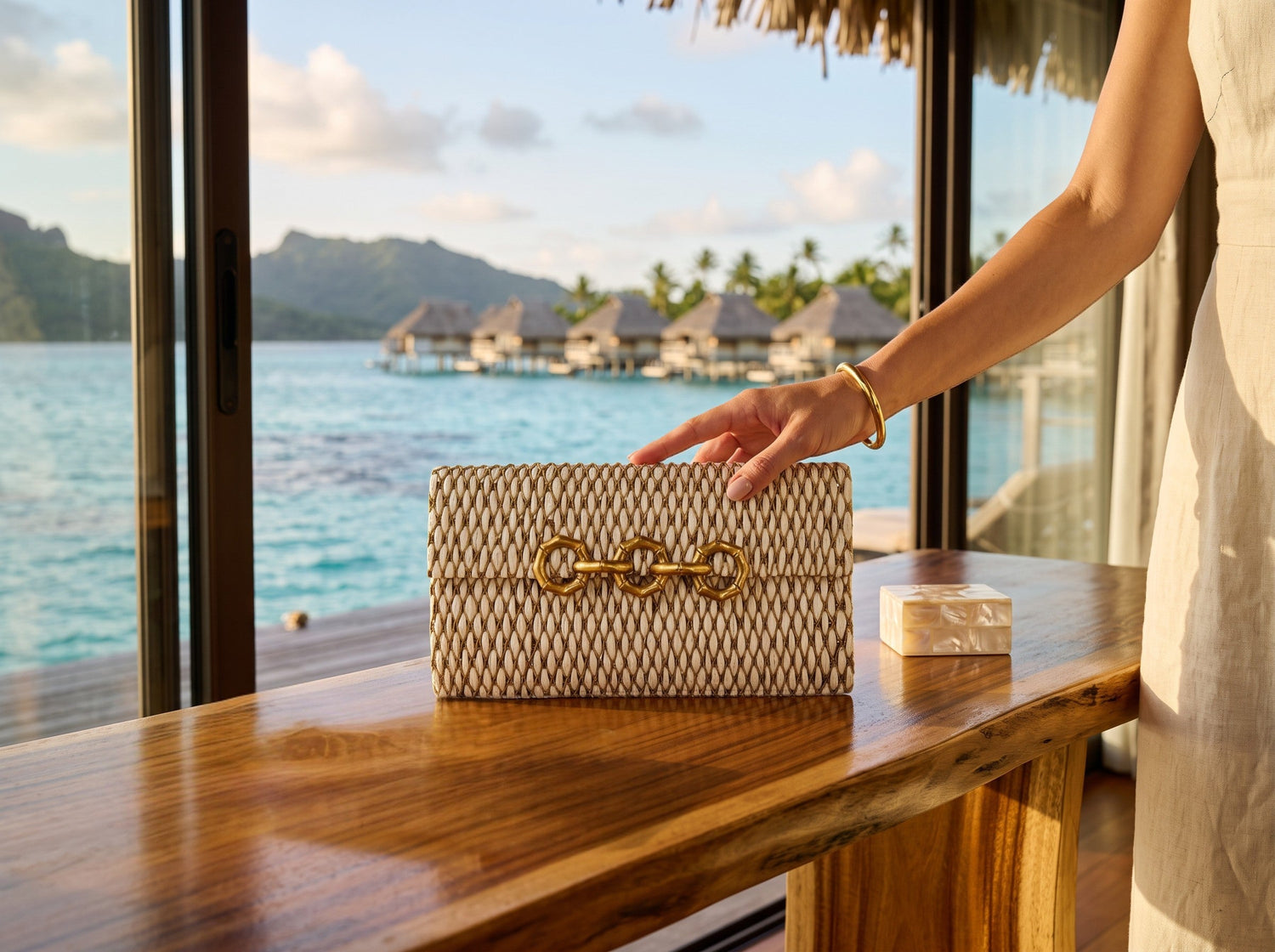 Trebor Style Seychelles cream raffia bag with metallic thread embroidery and a brass bamboo-inspired clasp on a desk.