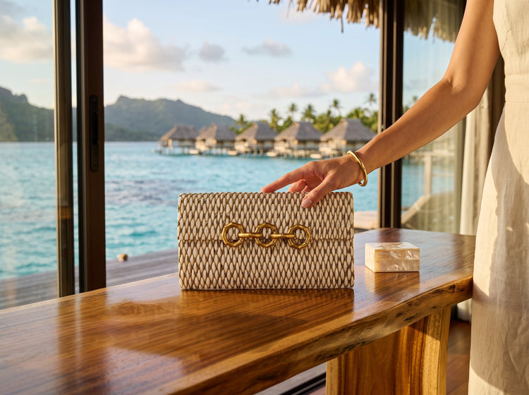 Trebor Style Seychelles cream raffia bag with metallic thread embroidery and a brass bamboo-inspired clasp on a desk.