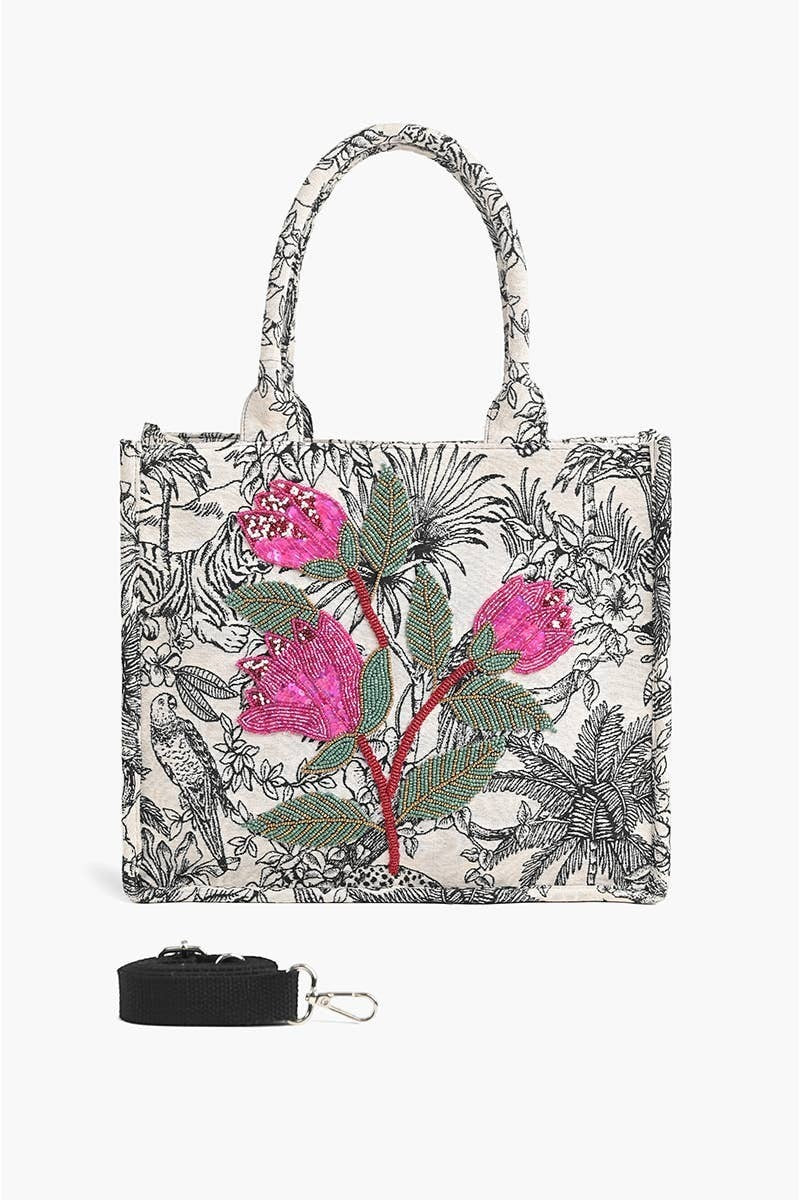 A tote bag with a black and white botanical and zebra print, decorated with pink flowers and green leaves, shown with a black detachable shoulder strap on a white background.