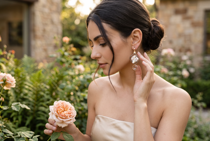 Trebor Style baroque pearl and pink quartz drop earrings with black diamond halo worn by a woman in a garden