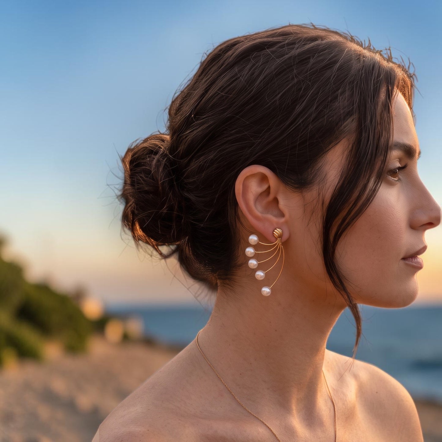 Trebor Style cascading pearl wire drop earrings in brushed gold worn by a woman at sunset by the ocean.