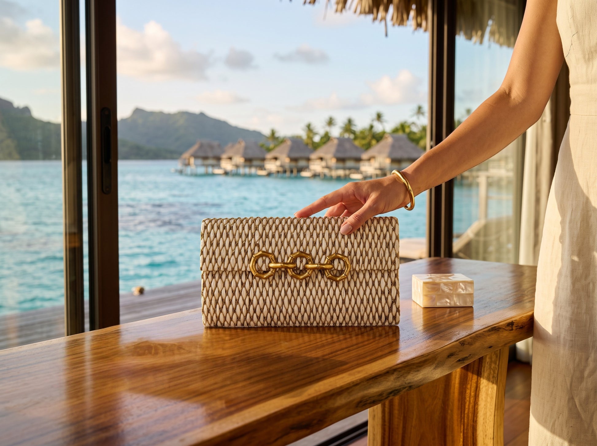 Trebor Style Seychelles cream raffia bag with metallic thread embroidery and a brass bamboo-inspired clasp on a desk.