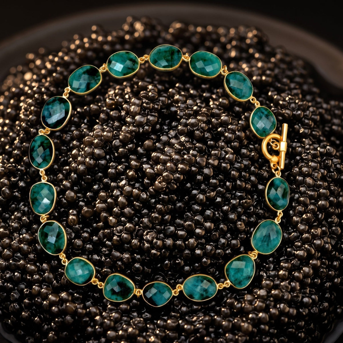 Trebor Style faceted oval emerald gemstone necklace with a vintage brass toggle closure on a dark beaded background.
