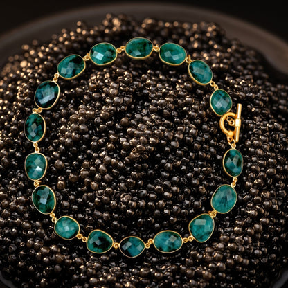 Trebor Style faceted oval emerald gemstone necklace with a vintage brass toggle closure on a dark beaded background.