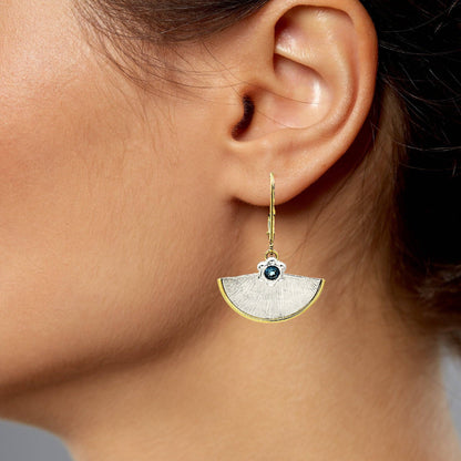 Trebor Style fan-shaped earring in sterling silver and 14kt gold with a London Blue Topaz worn on a woman's ear.
