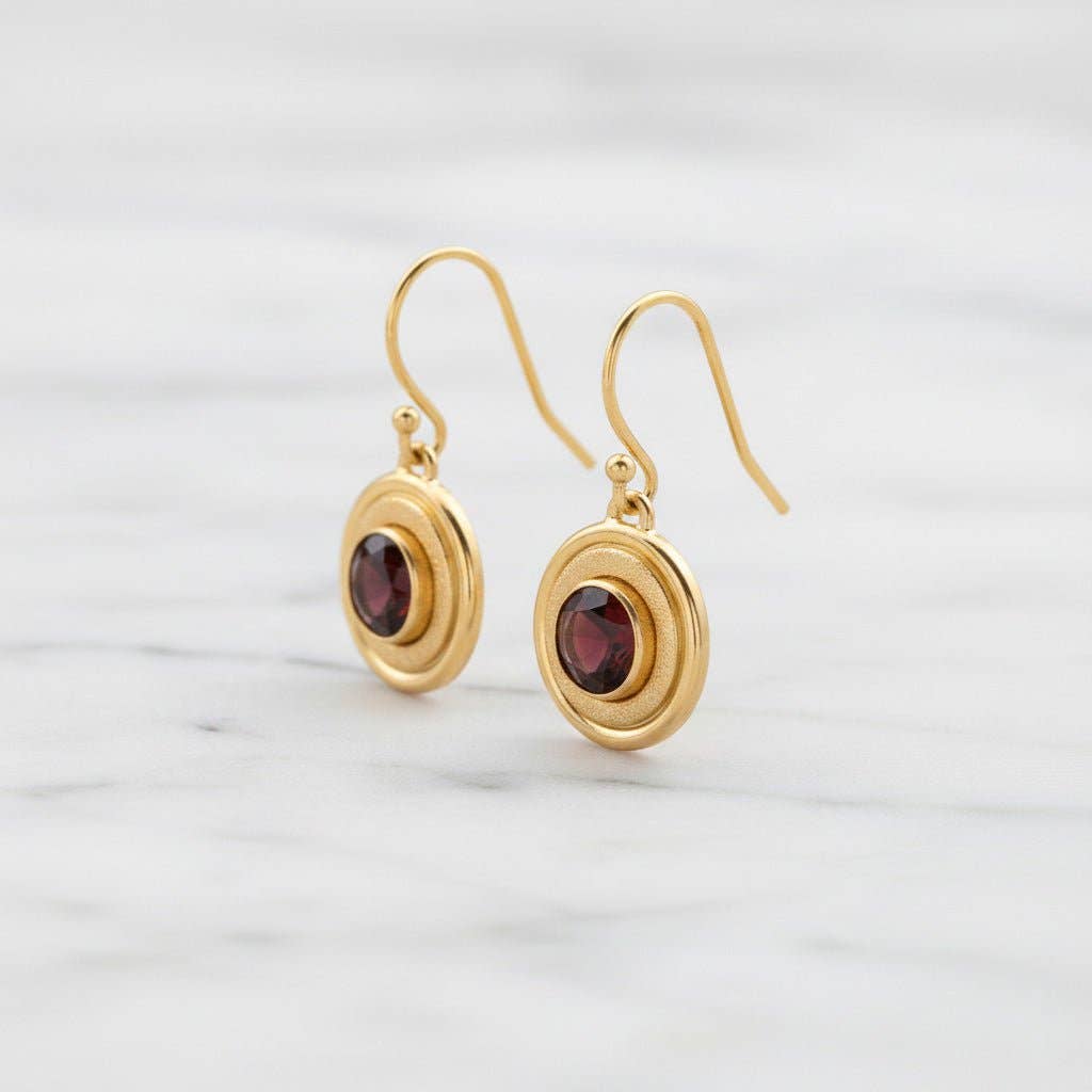 Trebor Style 14K gold-filled halo earrings featuring deep crimson 6mm garnet stones and textured concentric circles.