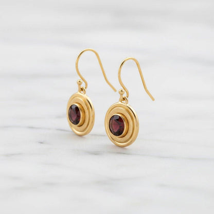 Trebor Style 14K gold-filled halo earrings featuring deep crimson 6mm garnet stones and textured concentric circles.