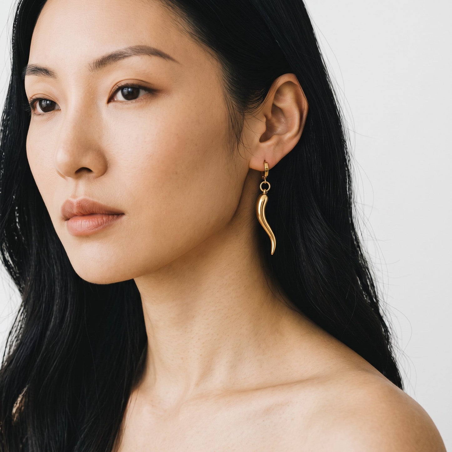 Trebor Style gold chili pepper charm hoop earrings worn by a model with long dark hair against a white background.