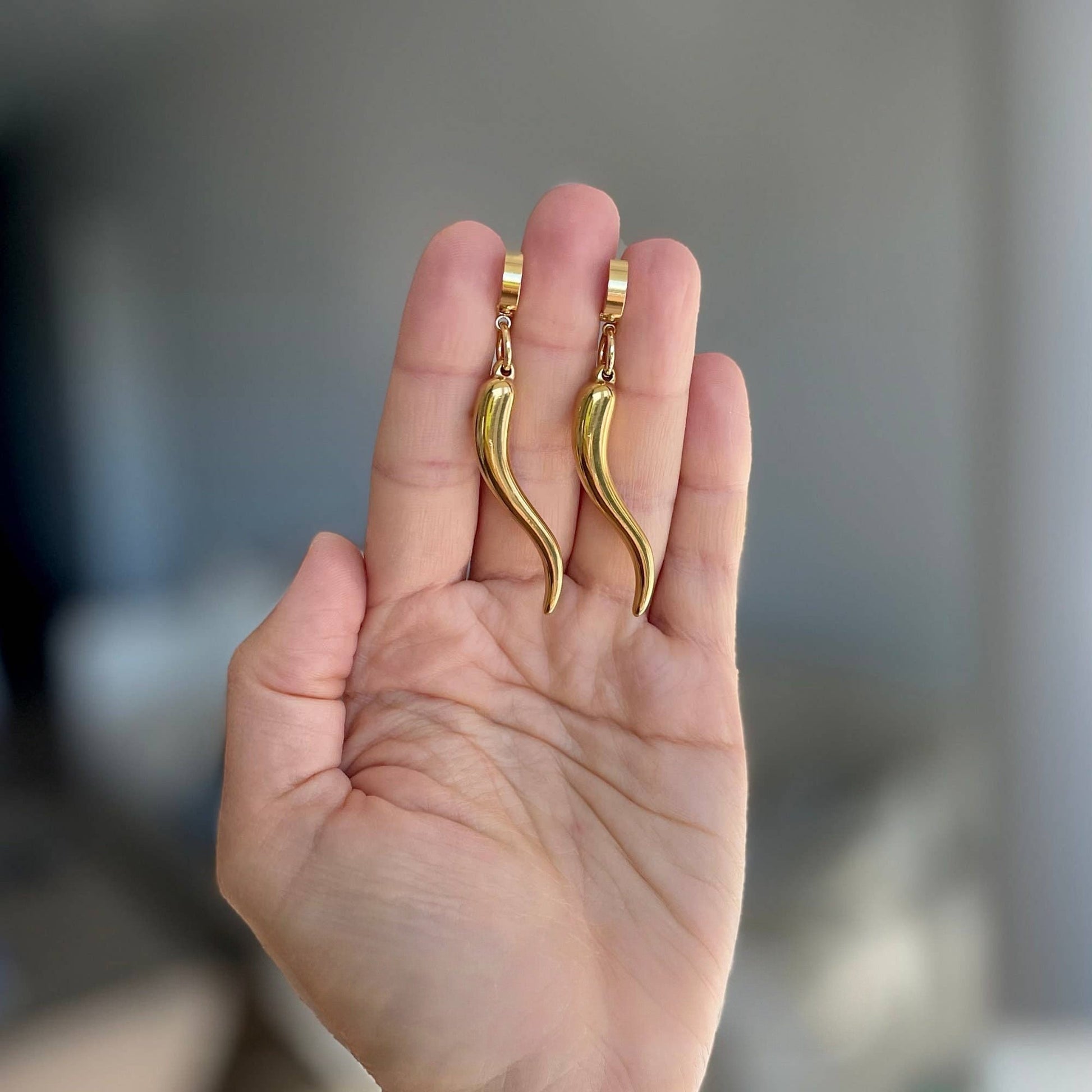 Trebor Style gold-filled chili pepper charms dangling from stainless steel hoop earrings held in a palm