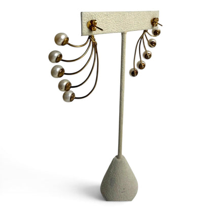 Trebor Style gold-tone fan-style statement earrings featuring five cascading cream faux pearls on a display stand.