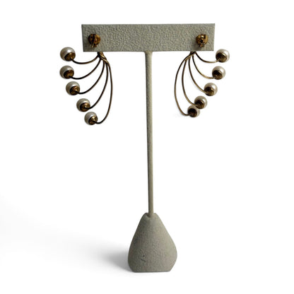 Trebor Style gold-tone fan-style statement earrings featuring five lustrous cream faux pearls on a display stand.
