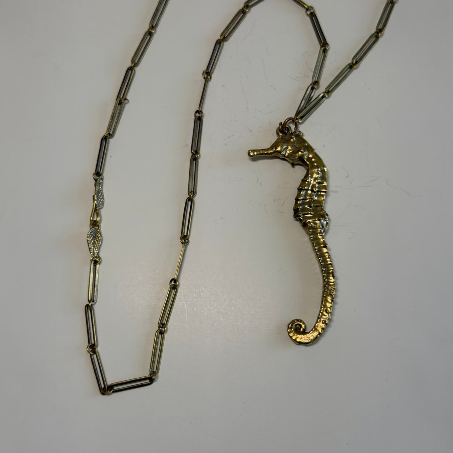 Trebor Style gold seahorse pendant necklace with a long link chain and intricate leaf clasp detail
