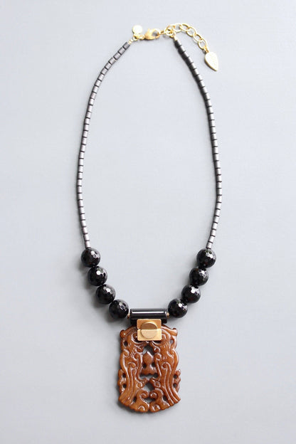 Trebor Style jade and black agate pendant necklace with hematite beads and gold-tone accents on a grey background.
