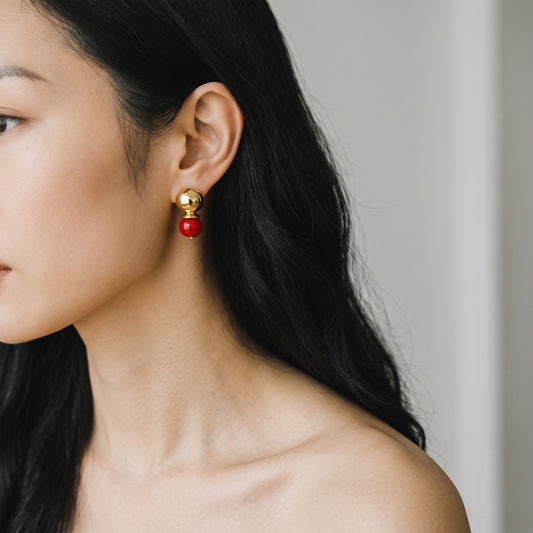 Trebor Style baby pebble orb earrings featuring a gold sphere and deep oxblood pearl on a model