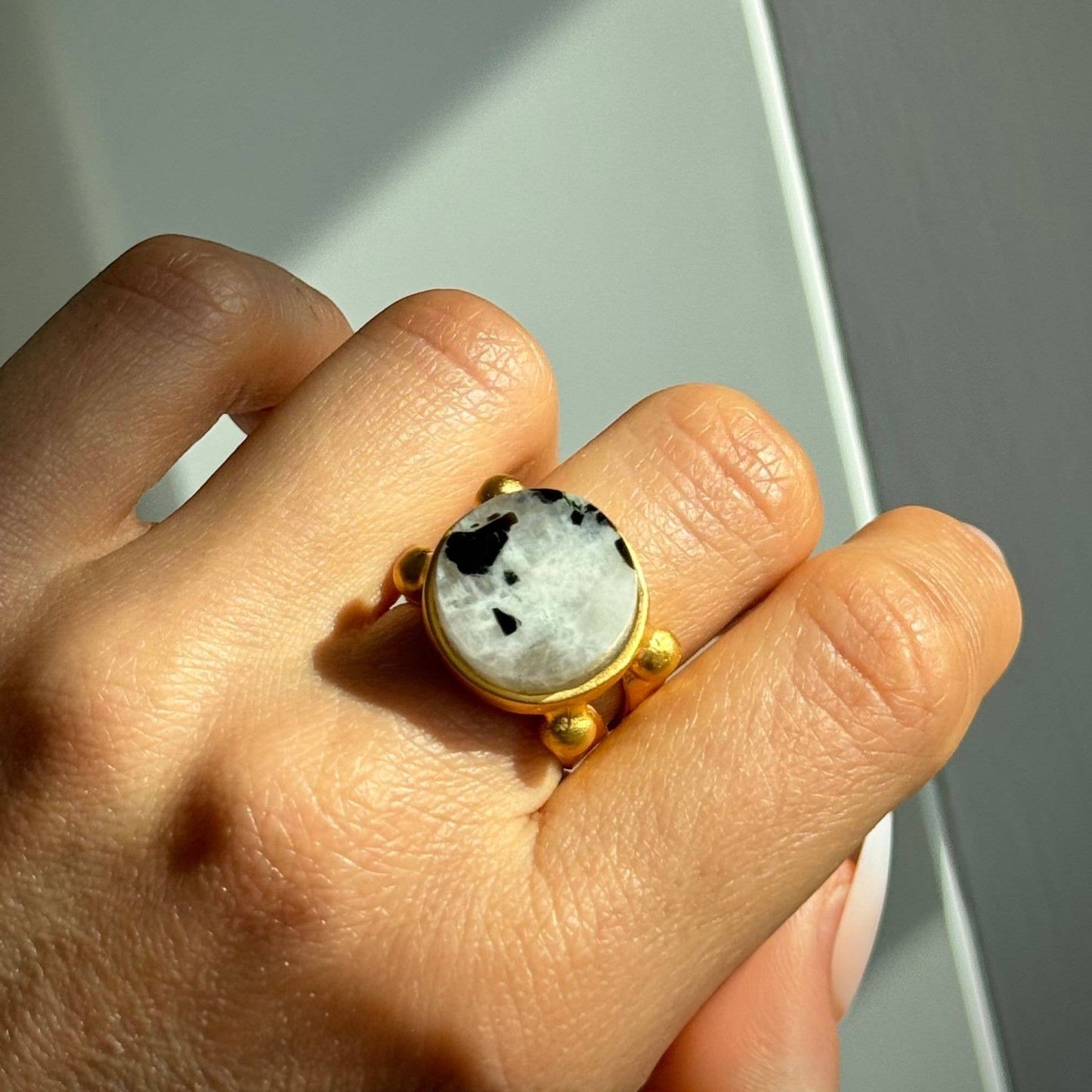 Trebor Style 16mm round moonstone ring with black inclusions set in a chunky gold filled adjustable band on a finger