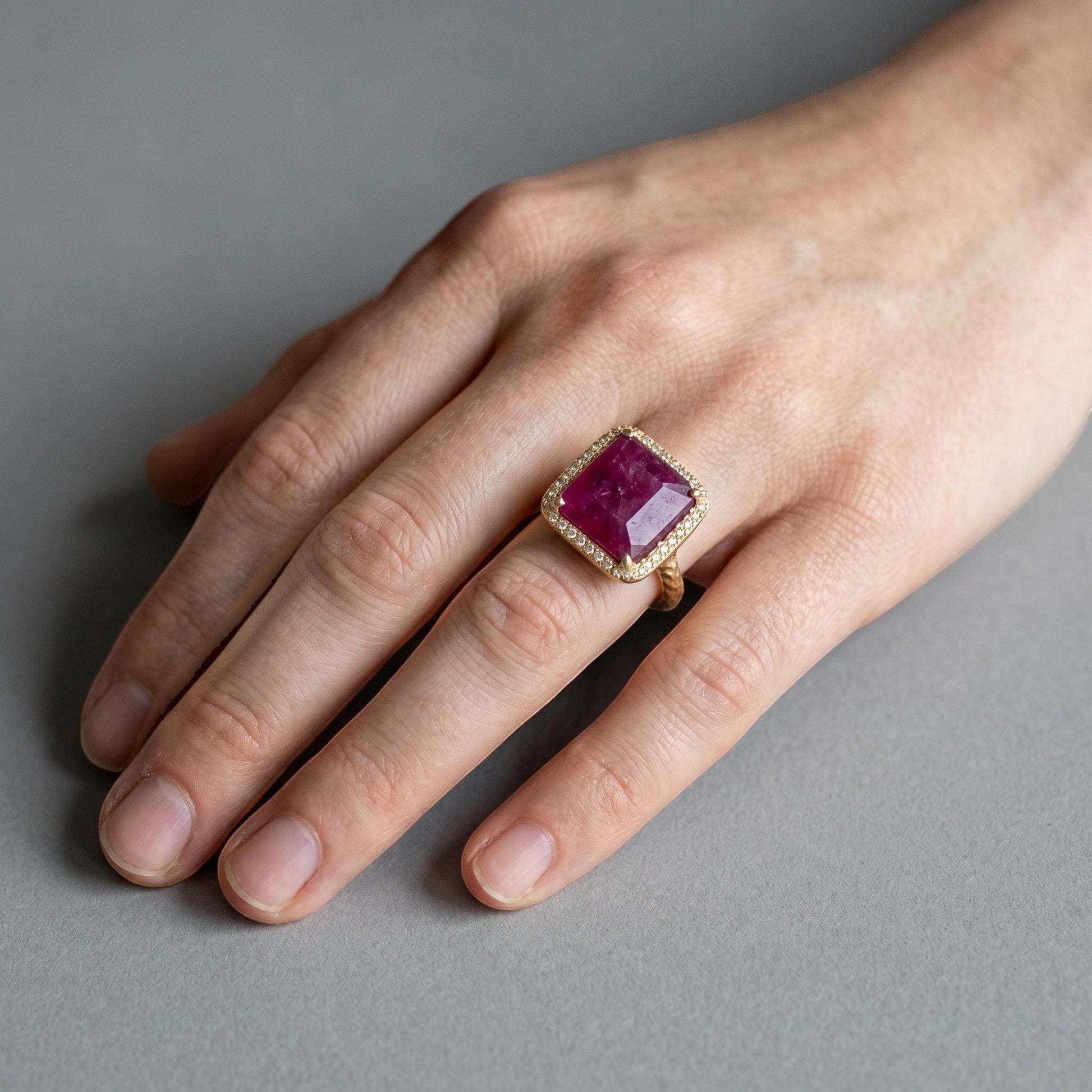 Trebor Style emerald-cut African ruby cocktail ring with a diamond pavé halo set in 14k gold on a woman's finger.