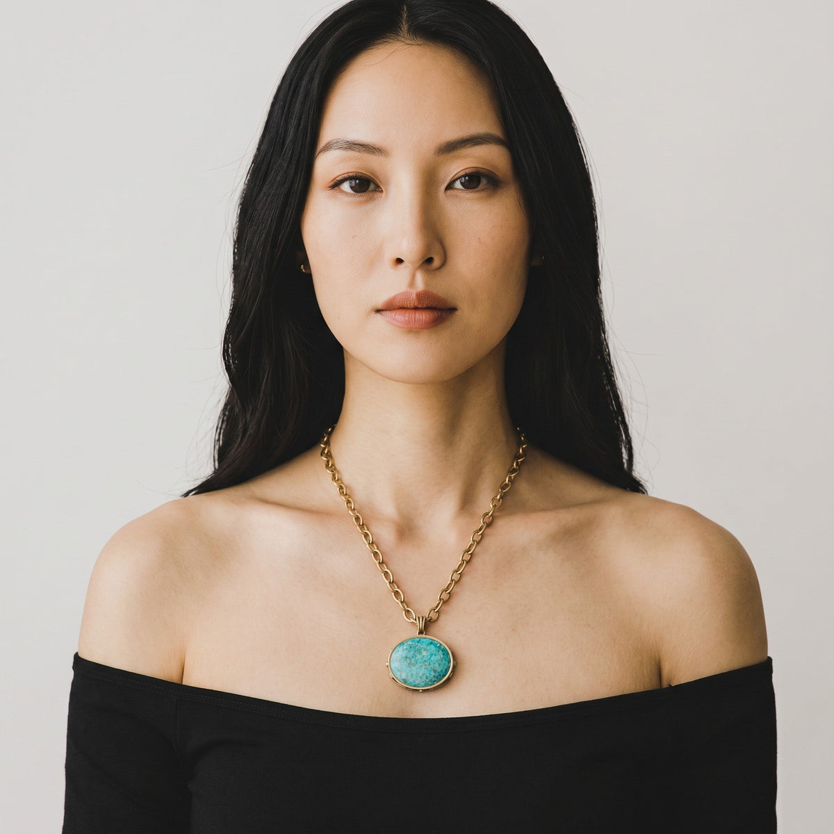 Trebor Style turquoise pendant necklace on a golden chain worn by a woman in a black off-shoulder top