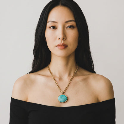 Trebor Style turquoise pendant necklace on a golden chain worn by a woman in a black off-shoulder top
