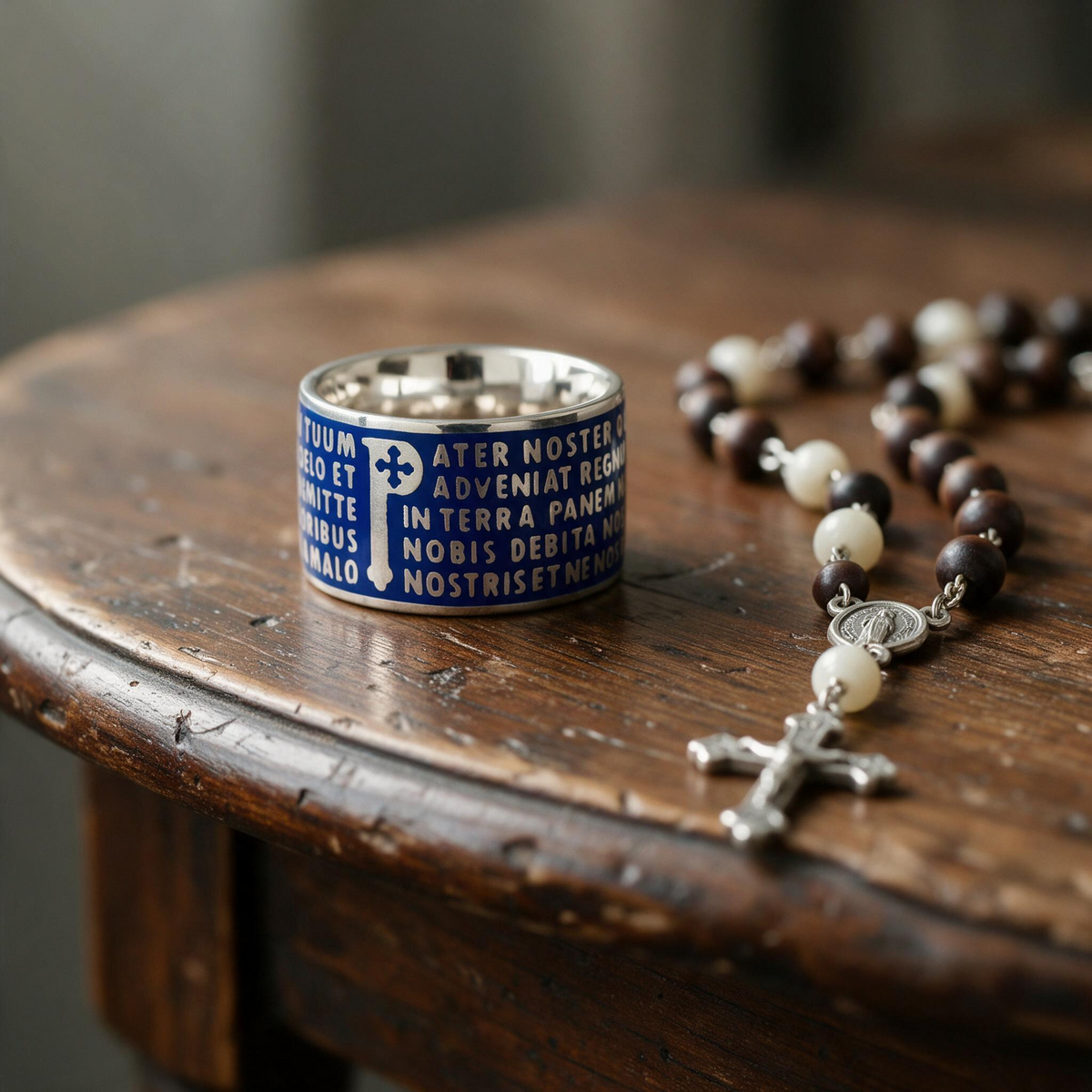 Trebor Style Tuum Animae Pater ring in sterling silver with blue enamel and embossed Latin text on a wooden table.