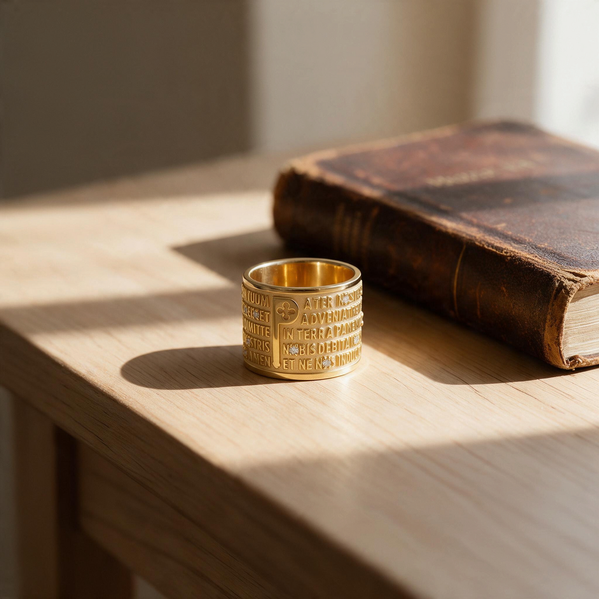 Trebor Style TUUM 18k yellow gold ring featuring engraved Latin Pater Noster text and diamond accents on a wooden table